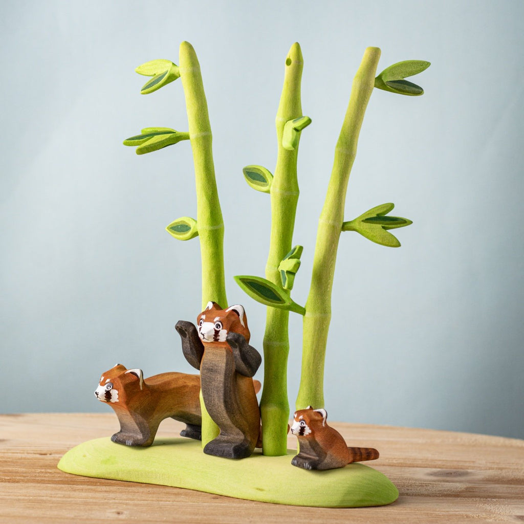 The Bumbu Handmade Wooden Red Panda Family with Bamboo Set features three handcrafted figures and tall bamboo stalks on a green base, making it perfect for Montessori learning and imaginative play on any wooden surface.