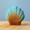 The Bumbu Handmade Wooden Big Shell with Pearl, featuring a blue and brown gradient finish, rests on a light wooden surface set against a simple pale blue backdrop.