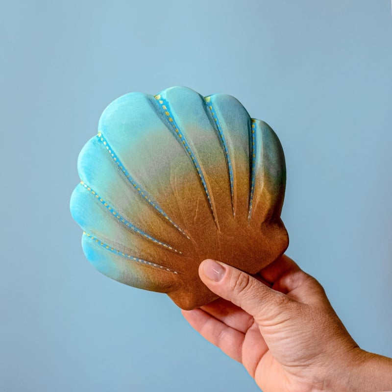 A hand holds the Bumbu Handmade Wooden Big Shell with Pearl against a plain light blue background.