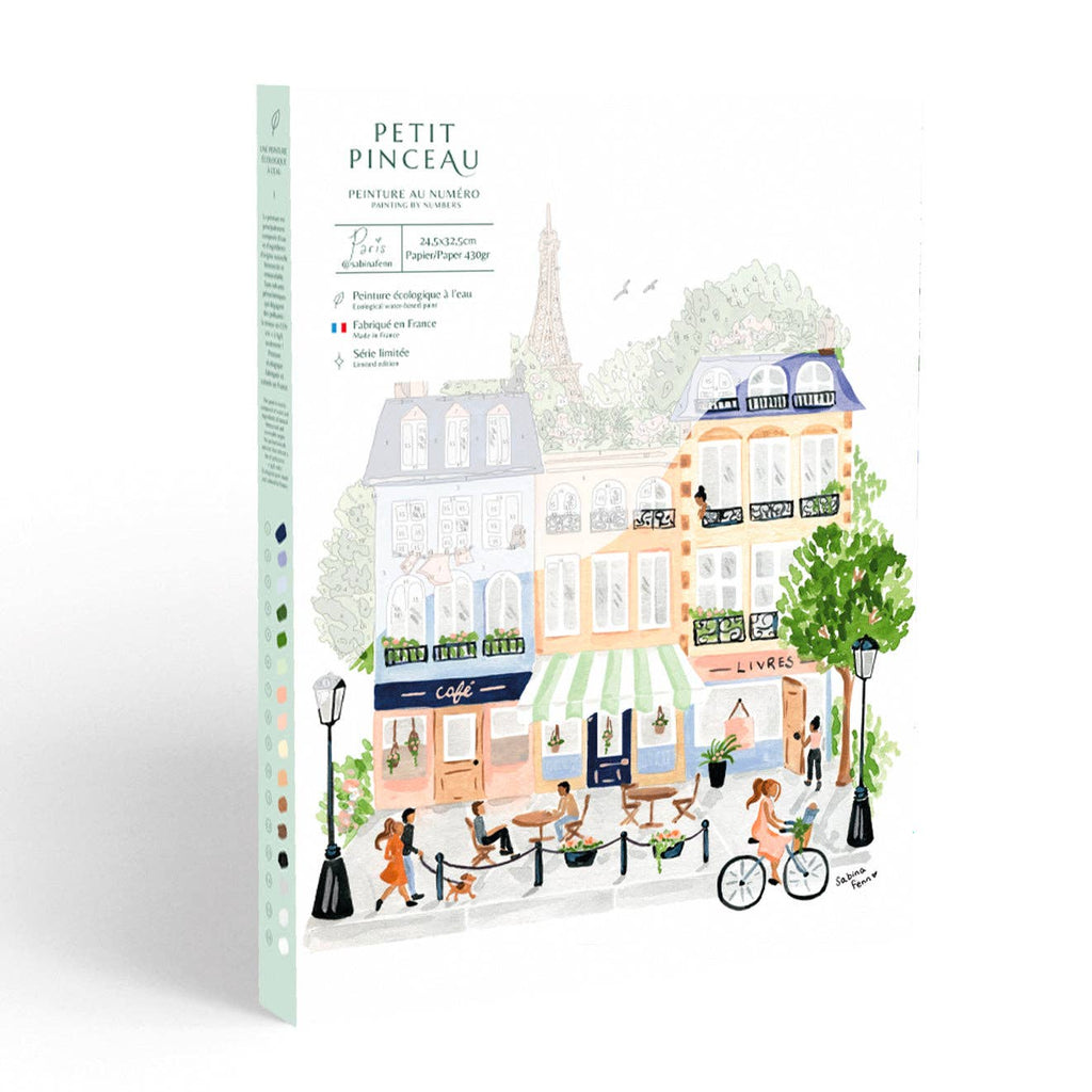 The Paint By Number Kit - Paris comes in an illustrated box with a lively Parisian street scene, people strolling, a café, bookstore, trees, and the Eiffel Tower—perfect for inspiring creativity in artists.