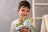 A young boy with short brown hair and freckles smiles while holding a Steiff Samu The Magic Dragon Plush Toy, 11 Inches, in a softly lit room decorated with stars on the gray wall behind him.