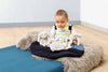 A baby in a white and yellow outfit smiles while sitting on a gray rug beside a blue mat, playing with three plush bunnies including the Steiff Hoppie Rabbit Security Blanket Baby Toy, 10 Inches.