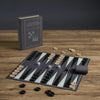 A Board Game: Checkers & Backgammon Vintage Bookshelf Edition set displayed on a wooden table with black and white pieces, dice, a black dice cup, and its stylish book-shaped case—a timeless treat for board game enthusiasts.
