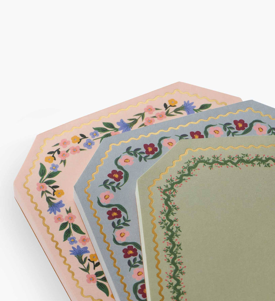 The Gemma Mini Notepad Trio features three decorative notepads with scalloped edges, metallic gold details, and pastel pink, blue, and green floral-bordered pages stacked on a white background.