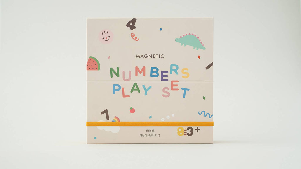 The Magnetic Number Play Set comes in a playful white box decorated with colorful numbers, cheerful faces, a dinosaur, fruit, and a yellow elastic band. This magnet puzzle set is ideal for children ages 3 and up.