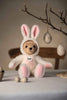 An 11-inch Steiff Teddy Bear with Bunny Hoodie Costume sits on a table, while decorative eggs hang from branches above, creating a festive atmosphere reminiscent of a zodiac lucky charm.