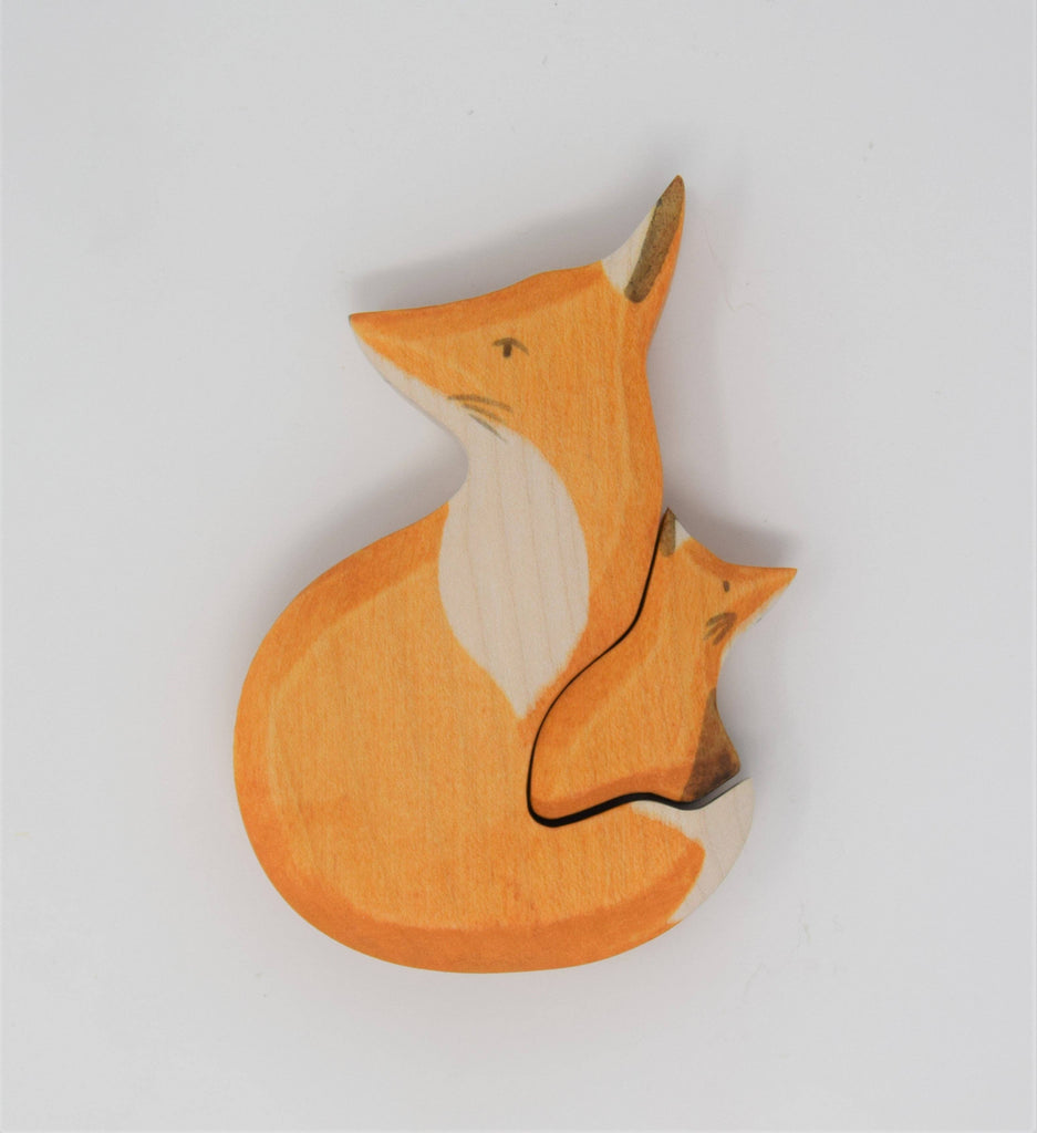 Handmade Wooden Snuggling Foxes: a sustainable hardwood toy puzzle with an orange fox and a smaller fox nestled inside, both featuring simple painted details and finished with natural, non-toxic stains. Set against a plain white background.