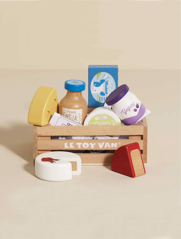 The Cheese & Dairy Wooden Market Crate includes assorted toy dairy items—cheese wedges, milk, cream, butter, and yogurt—in a colorful wooden crate for pretend play and learning.