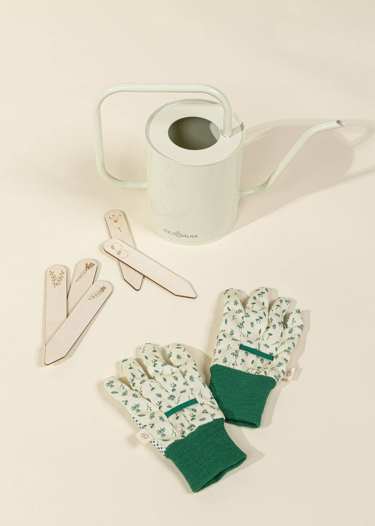 A Gardening Tools Playset, featuring a pale green watering can, floral garden gloves with green cuffs, and wooden plant markers, is arranged on a light beige surface.