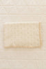 The Organic Pointelle Cotton Knit Baby Blanket, cream-colored with a scalloped lace edge and decorative holes, is beautifully made in Peru and shown folded on a quilted diamond-pattern cream bedspread.