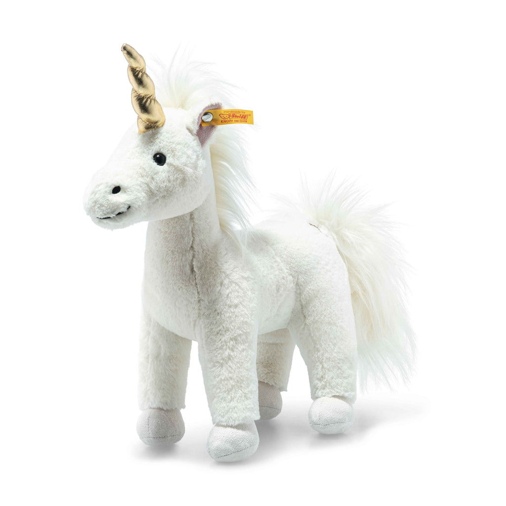 The Steiff Unica Unicorn Stuffed Plush Toy, 11 Inches, is a white plush unicorn with a gold horn, black eyes, fluffy mane and tail, stands upright on four legs, and has a yellow tag attached to one ear.