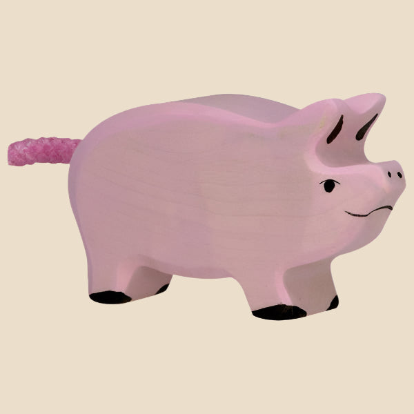 The Holztiger Piglet is a hand-carved pink wooden piglet with a curly tail, black hooves, and a small smile, shown on a beige background. Handcrafted in Europe and ships in one week.