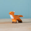 The Bumbu Handmade Wooden Fox Family Set includes a small wooden fox figurine, handcrafted in Romania with orange and white painted details, displayed on a light wood surface against a blue background.