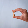 A hand holds a small kangaroo from the Bumbu Wooden Kangaroo Family Set, carved from sustainably sourced wood, upright between the thumb and index finger against a plain, light background.