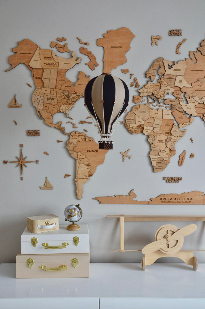 The Hot Air Balloon - Black, paired with a decorative wooden world map, travel-themed items like a globe, white suitcases, boxes, and a wooden airplane, creates the perfect decoration for a child's room.