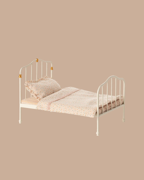 The PRE-ORDER: Vintage Bed, Mouse Size - Off White (ships early October), featuring a headboard and footboard, is dressed in light pink and white Maileg printed bedding with pillows, set against a plain beige background.