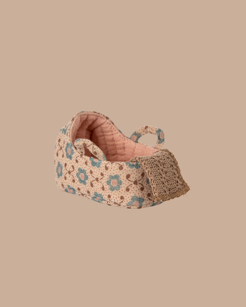 A small, fabric baby shoe with pink and beige tones, blue and brown florals, and lace detail—perfect for the PRE-ORDER: Carry Cot, Baby Mouse Size - Rose (ships late November)—displayed on a plain beige background.