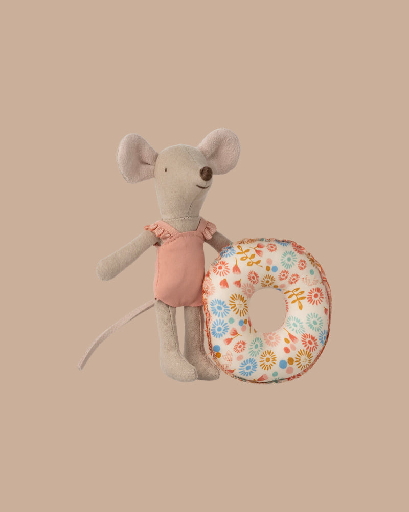 The Maileg Beach Mouse With Float, Little Sister - Flower features a small fabric mouse in a pink swimsuit holding a floral-patterned float, posed against a plain beige background.
