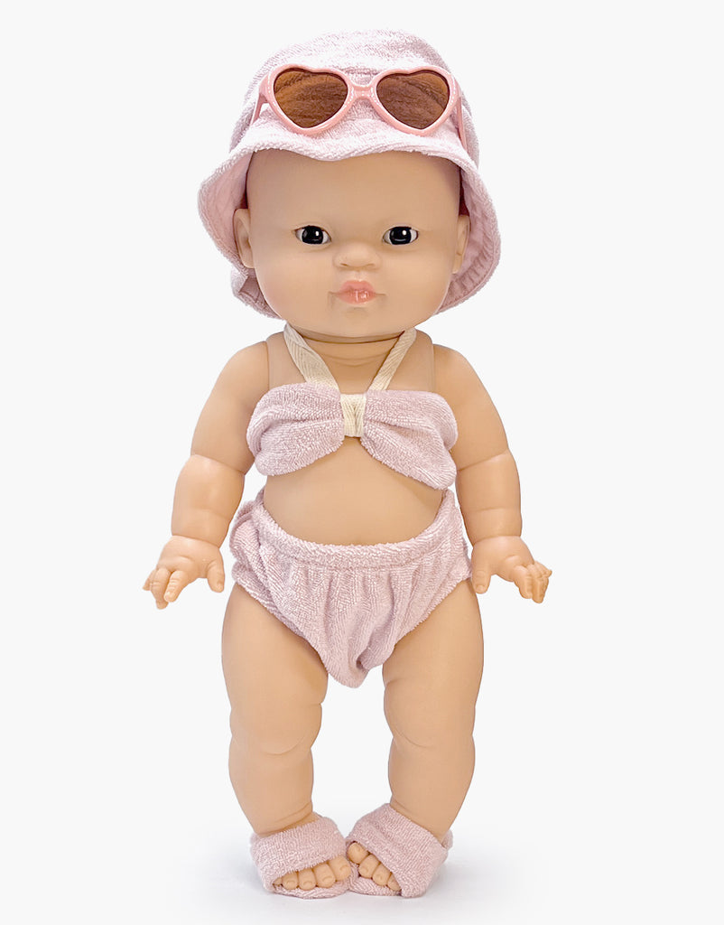 A Minikane doll models the Emile & Ida, Ursula 3-piece Swimsuit in terrycloth - Petal, featuring a matching bucket hat and heart-shaped sunglasses, standing upright against a white background.