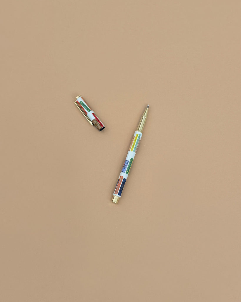 The Book Club Pen, featuring a gold cap and a vibrant patterned design, rests on a solid light brown background. Its cap is removed and positioned at the upper left of the pen.
