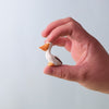 A hand delicately holds a Bumbu Handmade Wooden Pelicans Family Set toy, featuring an orange beak and white body—perfect for Montessori play—against a softly blurred, pale background.