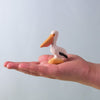 A hand holds a Bumbu Handmade Wooden Pelicans Family Set piece—a small wooden pelican with an orange beak and yellow base, designed for Montessori play—set against a plain light blue background.