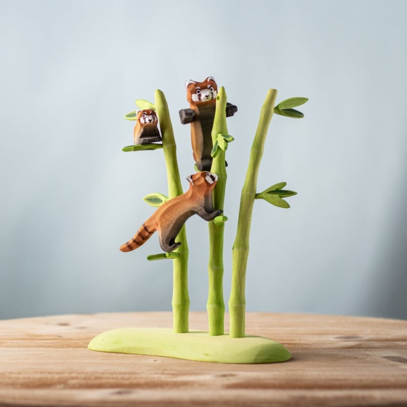 The Bumbu Handmade Wooden Red Panda Family with Bamboo Set features three small, smooth, handcrafted figures climbing and sitting on bamboo stalks—ideal as Montessori learning toys.