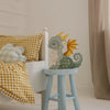 The Handmade Wooden Lamp - Dragon, Hunter Green sits on a blue stool by a bed with yellow gingham bedding and plaid pillows, making charming nursery decor and a delightful children's night light in this cozy bedroom.