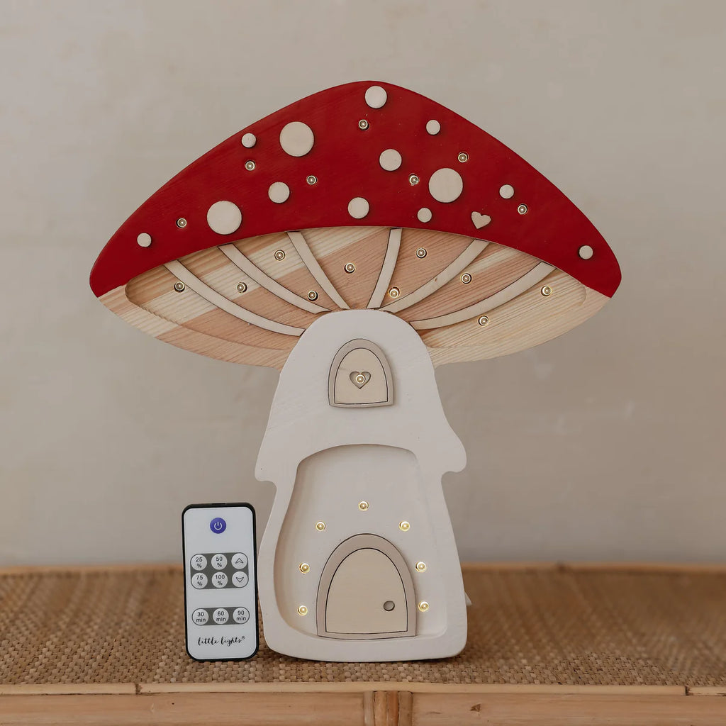 The Handmade Wooden Lamp - Mushroom House is crafted from natural pinewood with a red cap, white spots, and heart-shaped door details. Ideal as a children's night light, it comes with a remote control and rests on a woven surface.