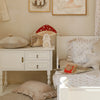A cozy, vintage-style children's room with off-white furniture, plush pillows, soft bedding, whimsical animal artwork, natural pinewood accents, and a Handmade Wooden Lamp - Mushroom House as a charming children's night light.