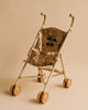 The Konges Sloejd Sparkly Sequin Doll Stroller - Golden Cherry features tan wheels and handles, a shiny gold sequined seat with a cherry design, and a matching beige background.