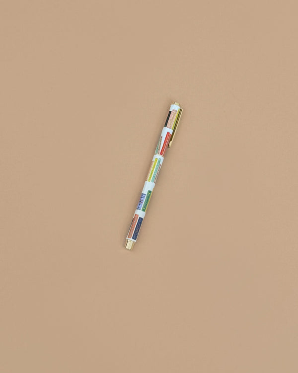 The Book Club Pen, a vibrant multi-colored rollerball, is positioned diagonally against a plain beige background.