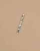 The Book Club Pen, a vibrant multi-colored rollerball, is positioned diagonally against a plain beige background.