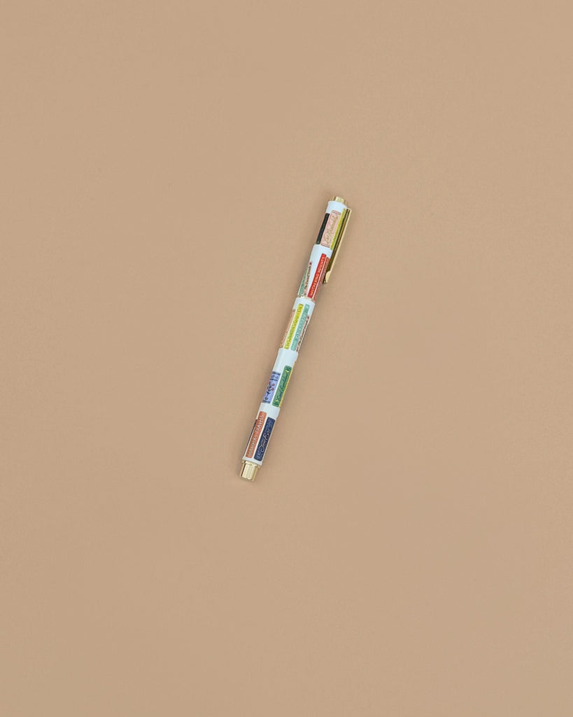 The Book Club Pen, a vibrant multi-colored rollerball, is positioned diagonally against a plain beige background.