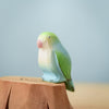 The Bumbu Handmade Wooden Tree Stump and Lovebirds Set features a pastel-colored bird figurine in green and light blue, perched on a carved wooden stump, part of a handcrafted nature toy collection against a light blue backdrop.