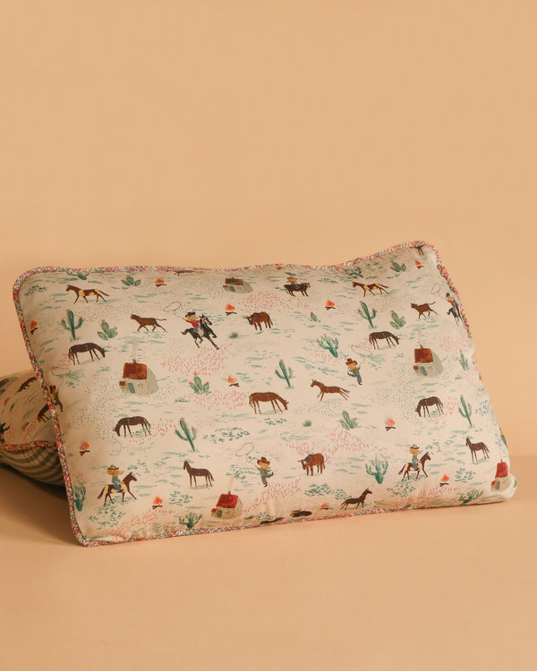 The Maileg Cushion - Pony is a rectangular 100% cotton cushion with a playful Western-themed print of cowboys, horses, cacti, and cabins on a beige background, perfectly matching any beige surface.