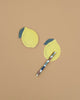 Two Lemon Sticky Notes in die-cut shapes and a multicolored pen are displayed on a plain light brown surface, with one sticky note placed above the pen and the other below it.