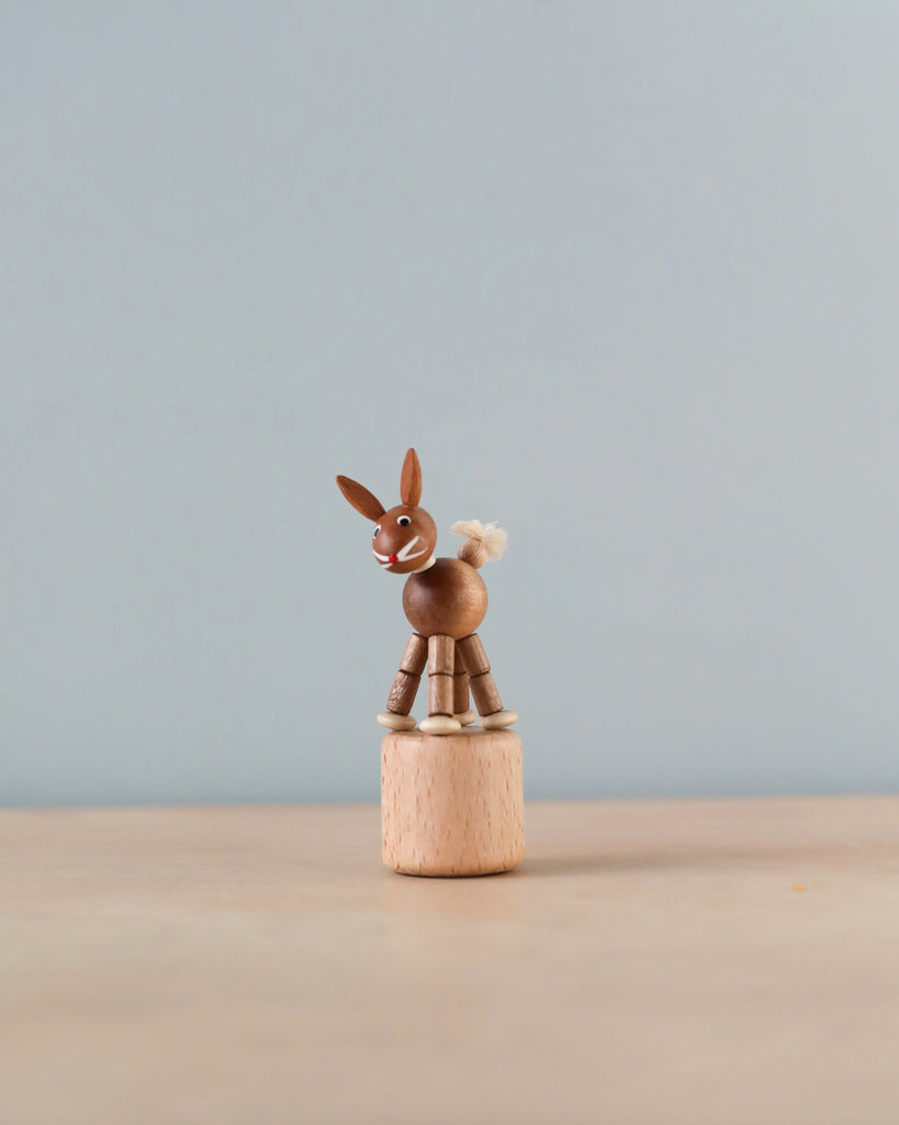 A Wobbly Rabbit Push Toy with articulated limbs and a fluffy tail, handmade in Germany, standing on a small wooden spool against a light gray background.