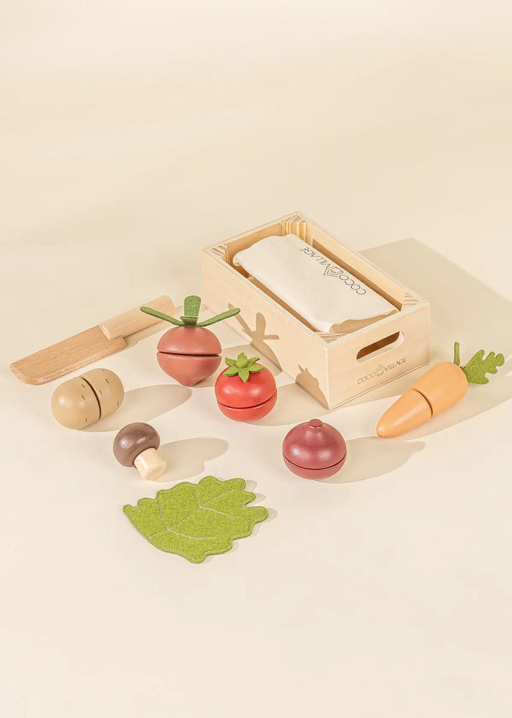 Sliceable wooden vegetable toys laying flat with a wooden crate and wooden knife.
