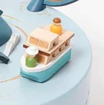 A miniature wooden Boat Replacement for Whale Music Box with a white hull and blue base, featured on a light blue surface, adorned with small, colorful details like a green bottle and an orange object on deck. This listing is