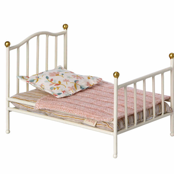 A Maileg Miniature Bed with golden knobs, adorned with a pink knitted blanket and a floral pillow.