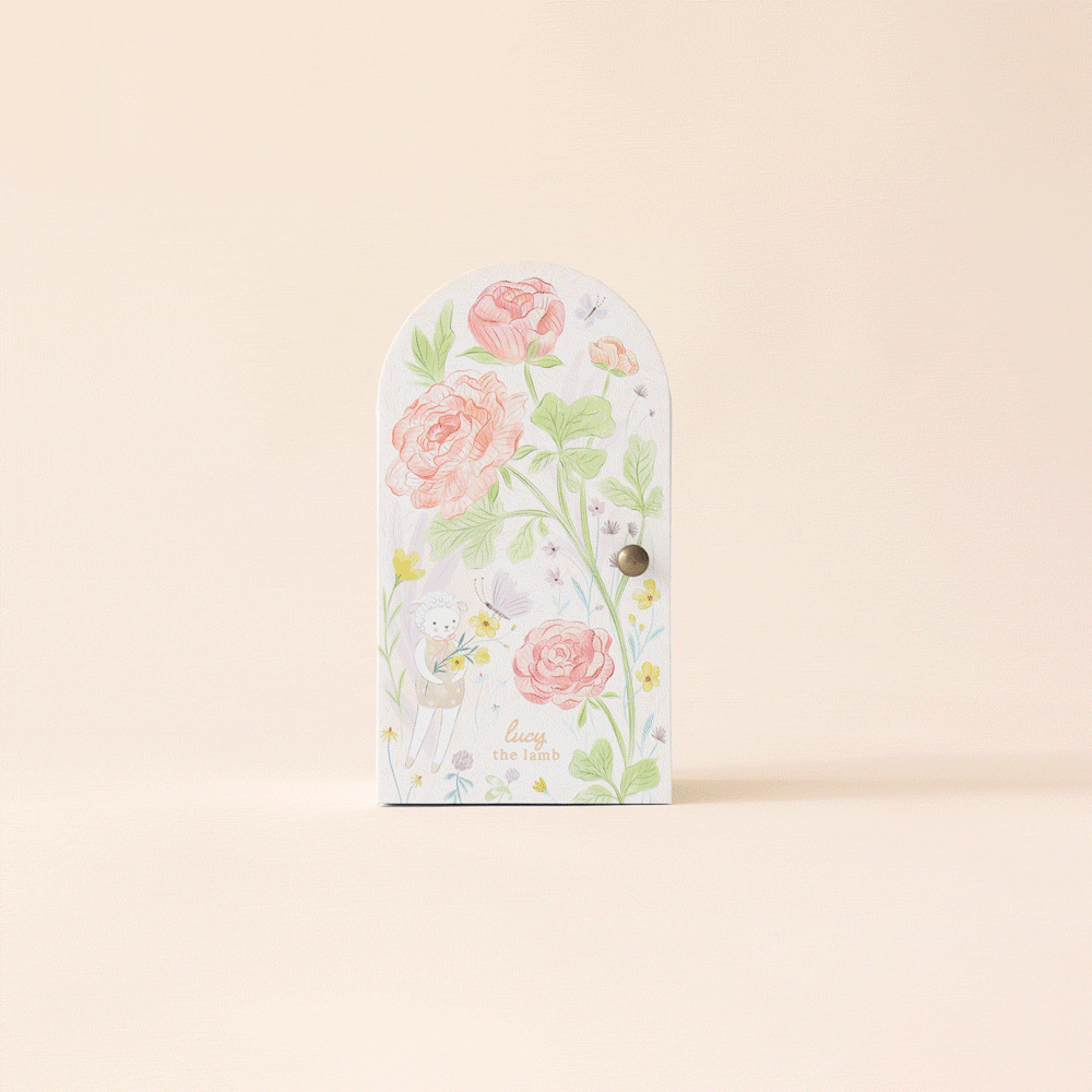 Textured with floral designs and a small lamb figure, the decorative door is reminiscent of Cuddle + Kind Tiny Lucy the Lamb. It features pink roses, green leaves, and a whimsical lamb on a soft beige background for a charming, playful vibe.