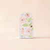 A handmade Peruvian card features an illustrated flamingo, pink flowers, and green leaves on a soft peach background. It’s designed with an arched window style and a golden knob on the right.