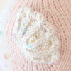 Close-up of a hand-knit piece made from natural Peruvian cotton yarn in powder pink, with a white textured pattern and pastel speckles. It likely displays cute baby animals, perhaps as part of the Cuddle + Kind Baby Seahorse (Powder Pink) garment or collectible accessory.