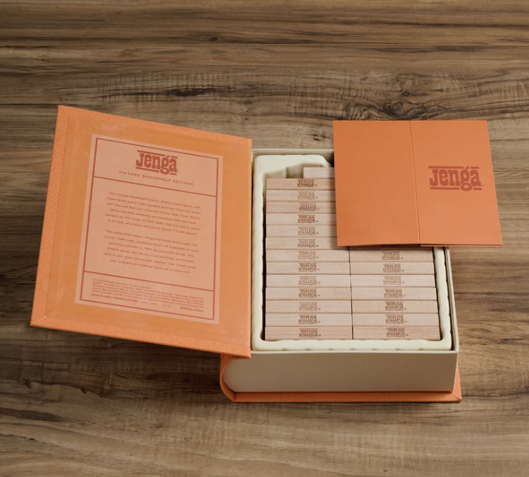 The Jenga Vintage Bookshelf Edition sits open on a wooden surface, showing neatly stacked blocks inside its orange book-shaped box—making it perfect for family game night.