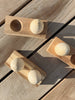 Three Wooden Egg Shakers with Stand rest on a wooden surface, casting gentle shadows in the sunlight. Perfect for encouraging developmental milestones, each shaker features a natural wood finish and is displayed on its sleek stand.