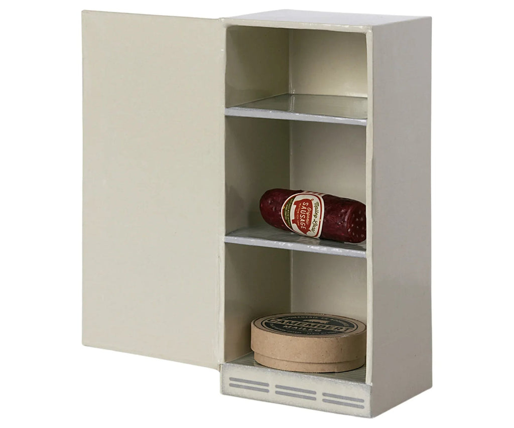 A miniature white cabinet from the Maileg Kitchen Set has one door open, revealing three shelves: the top shelf displays a labeled salami, the bottom shelf holds a round container, while the middle shelf awaits treasures. Ideal for any Maileg Kitchen setup!.