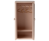 The Maileg Nursery Set offers a small light pink wardrobe for mouse families, with two compartments. The upper section includes three gold wire hangers, while the lower is empty. It features round handles on each side, making it an ideal addition to dollhouses for any Maileg fan.