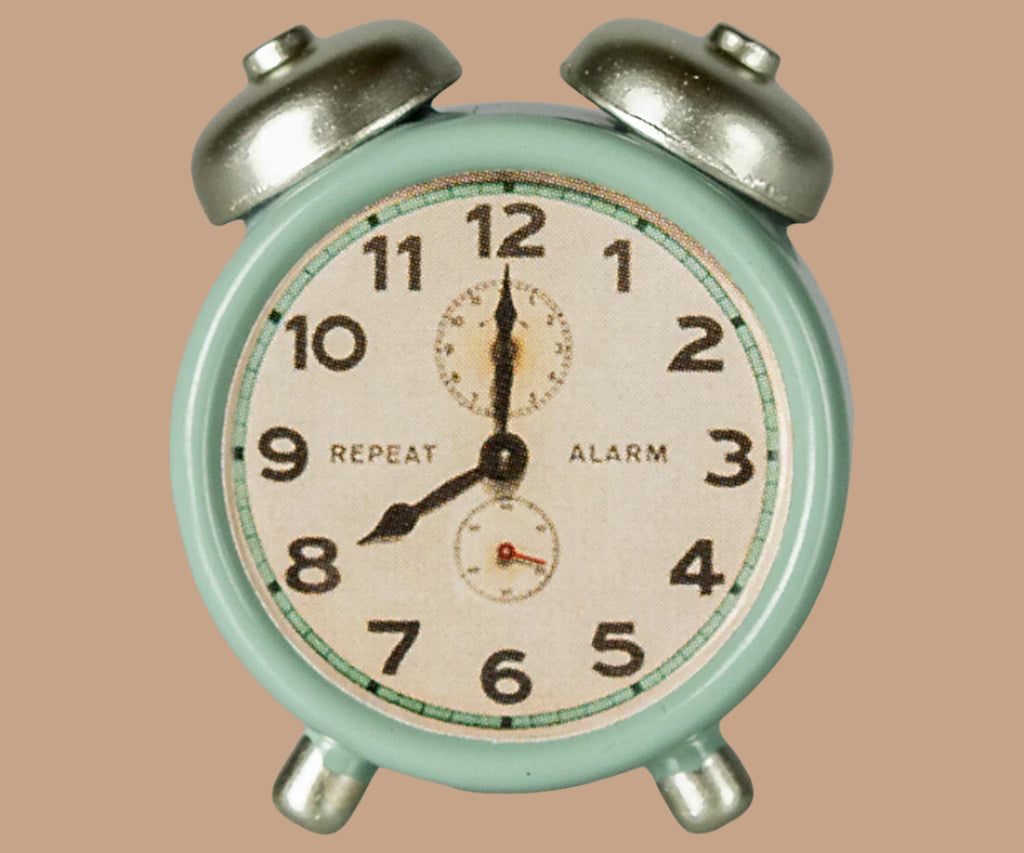 A vintage light blue twin-bell alarm clock showing 8:00 sits beside the Maileg Little Sister Bedtime Set, both placed on a plain beige background.