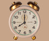 A vintage white and gold analog alarm clock with twin bells and black numbers on its face, set against a beige background—pairs perfectly with your Maileg Moms Afternoon Tea Set display.